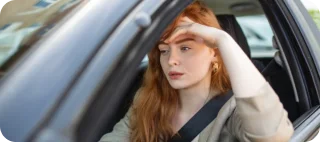 Woman sitting in a car, with her hand on her forehead