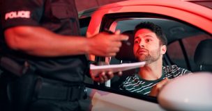 Driver looks worried as a police officer writes a citation during a nighttime traffic stop, highlighting most common traffic violations that raise insurance rates.