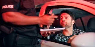 Driver looks worried as a police officer writes a citation during a nighttime traffic stop, highlighting most common traffic violations that raise insurance rates.