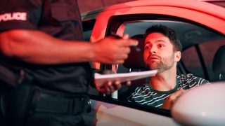 Driver looks worried as a police officer writes a citation during a nighttime traffic stop, highlighting most common traffic violations that raise insurance rates.