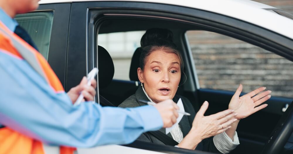 Driver reacts while an officer writes a citation during a traffic stop, highlighting most common traffic violations that raise insurance rates.