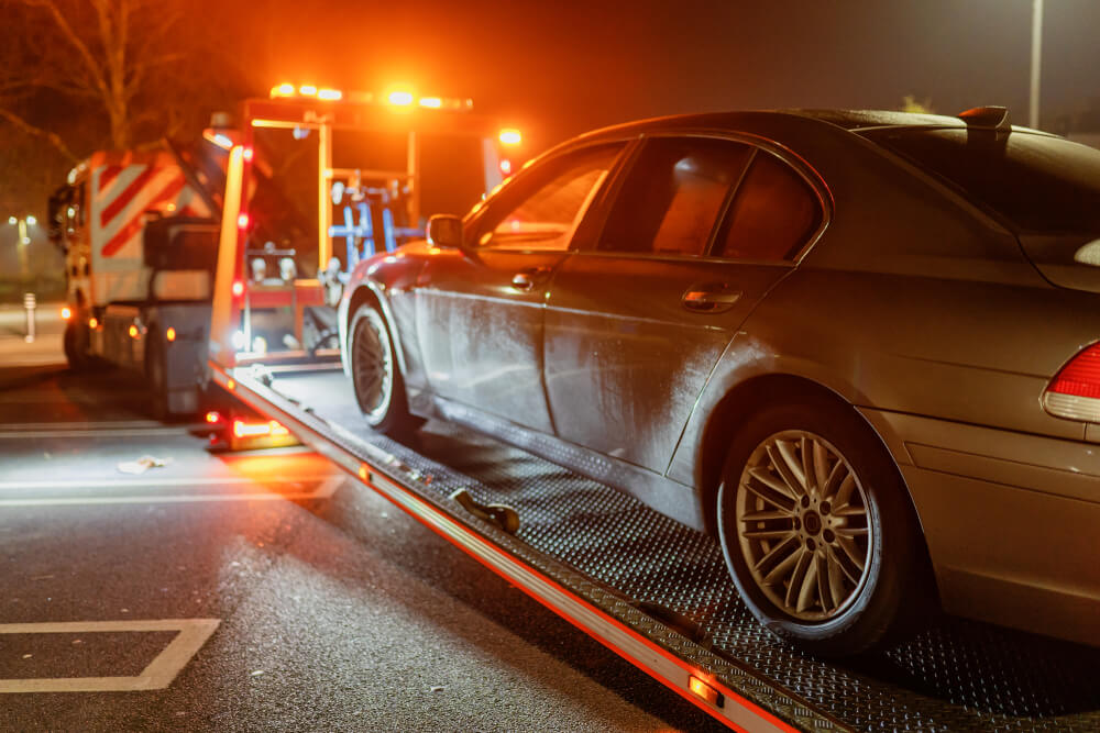 Car being loaded onto a tow truck at night after a breakdown, showing how roadside assistance coverage can help when drivers need emergency towing.