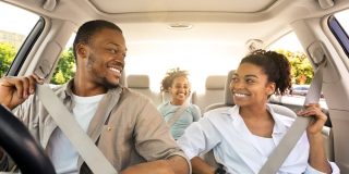 Smiling family of three rides in a car with everyone buckled up, illustrating seat belt safety laws.