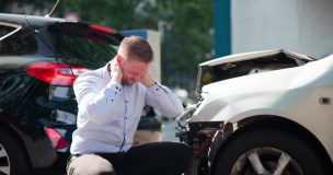 Man sits beside two damaged cars after a crash, showing how **liability insurance** can help when an accident leads to injury or property damage claims.