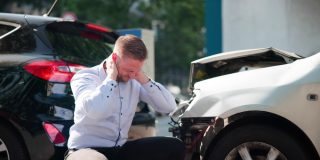 Man sits beside two damaged cars after a crash, showing how **liability insurance** can help when an accident leads to injury or property damage claims.