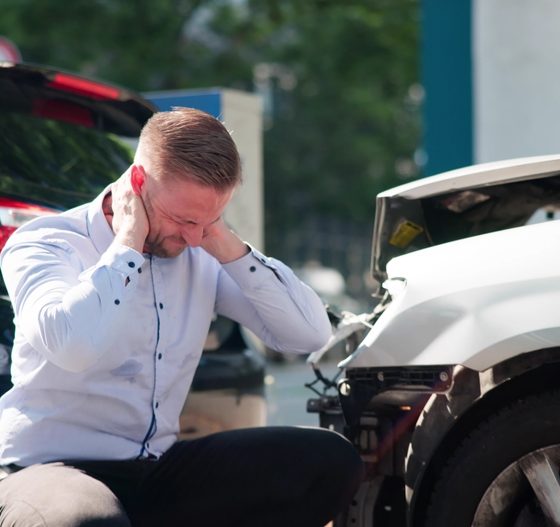Man sits beside two damaged cars after a crash, showing how **liability insurance** can help when an accident leads to injury or property damage claims.