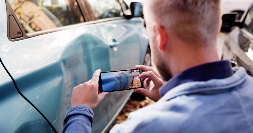 Man takes a photo of damage on a car door after an accident, showing how liability insurance can help when property damage claims are involved.