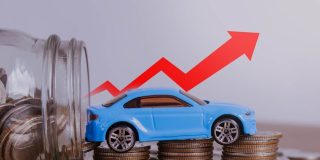 Blue toy car sits on stacks of coins beside a jar of change, with a red arrow pointing upward to show costs rising and car insurance going up.