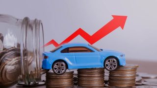 Blue toy car sits on stacks of coins beside a jar of change, with a red arrow pointing upward to show costs rising and car insurance going up.
