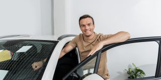 Man standing next to a new car, illustrating insurance coverages for a new car and vehicle protection