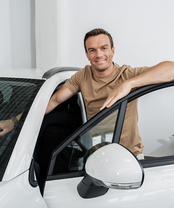 Man standing next to a new car, illustrating insurance coverages for a new car and vehicle protection