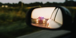 Police vehicle visible in a driver's side mirror during a traffic stop after receiving a speeding ticket.