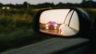 Police vehicle visible in a driver's side mirror during a traffic stop after receiving a speeding ticket.