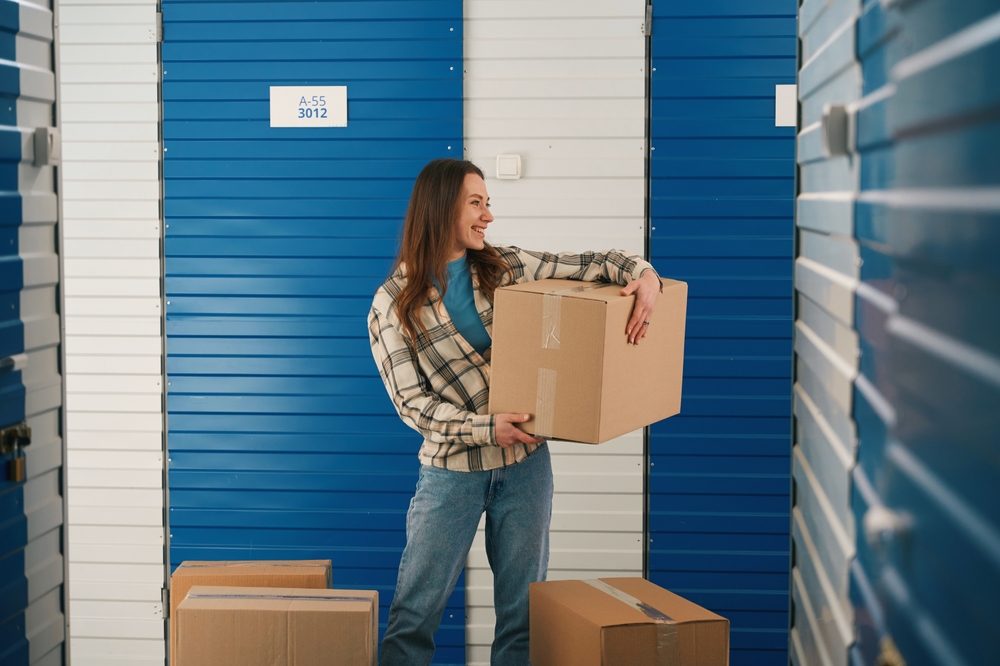 Woman carrying a cardboard box outside a storage unit.