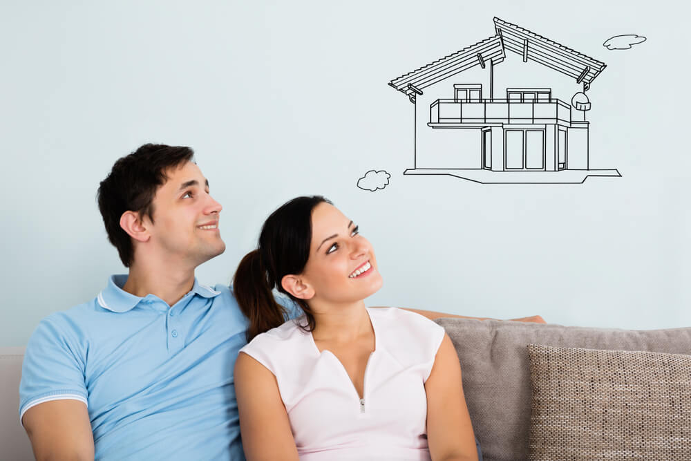Smiling Young Couple Sitting On Sofa Thinking Of Getting Their New House - cheap home insurance.
