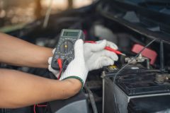 Using a voltage meter to check the power in a car battery under the hood.