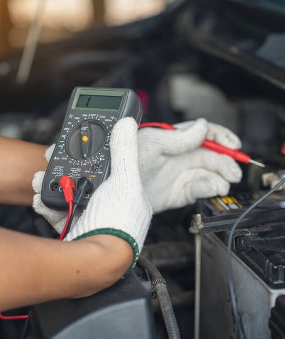 Using a voltage meter to check the power in a car battery under the hood.
