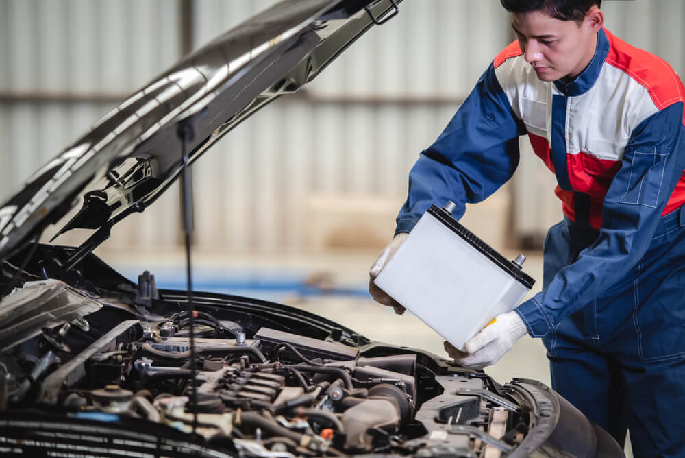 Mechanic replaces a battery in the engine of a vehicle.