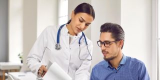 Female doctor showing test results to male patient in medical clinic. General practitioner consulting male client at medical checkup visit in hospital. Medicine and healthcare concept, free or low-cost health insurance in California.