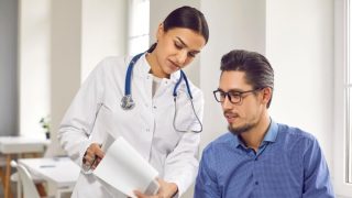 Female doctor showing test results to male patient in medical clinic. General practitioner consulting male client at medical checkup visit in hospital. Medicine and healthcare concept, free or low-cost health insurance in California.