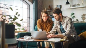 Couple sits on couch and works on choosing the right business insurance for their small company.