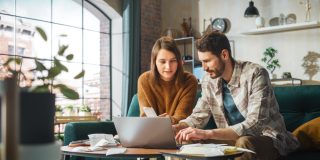 Couple sits on couch and works on choosing the right business insurance for their small company.