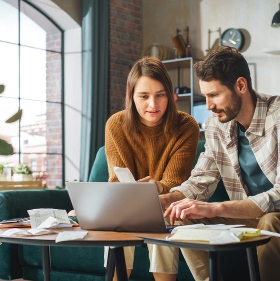 Couple sits on couch and works on choosing the right business insurance for their small company.