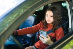 Female teenage driver using a smartphone while behind the wheel, highlighting the dangers of distracted driving and road safety concerns