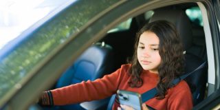 Female teenage driver using a smartphone while behind the wheel, highlighting the dangers of distracted driving and road safety concerns