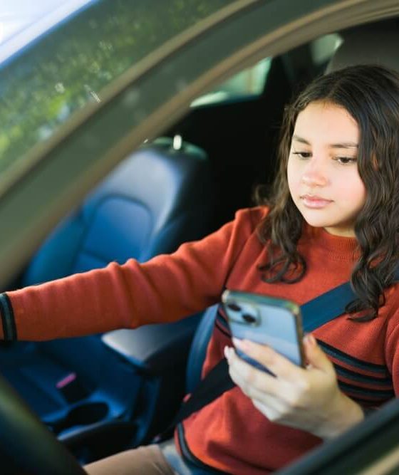 Female teenage driver using a smartphone while behind the wheel, highlighting the dangers of distracted driving and road safety concerns
