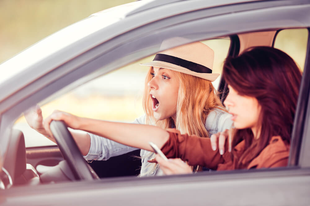 Woman driving a car and typing on a smart phone. Dangerous driving. Passenger yelling in alarm before wreck due to distracted driving.