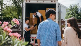 Assisted by a professional delivery team a couple transitions to their new home. Together they unload and lift cardboard boxes ensuring an organized and efficient move to their new rental home with transferred renters insurance.