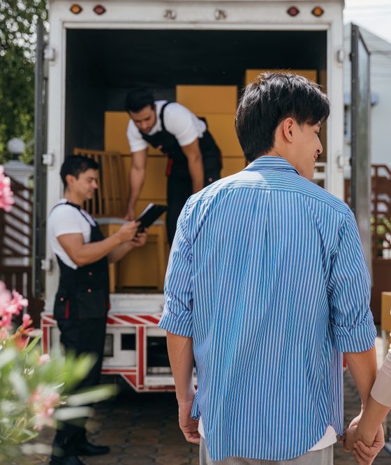 Assisted by a professional delivery team a couple transitions to their new home. Together they unload and lift cardboard boxes ensuring an organized and efficient move to their new rental home with transferred renters insurance.