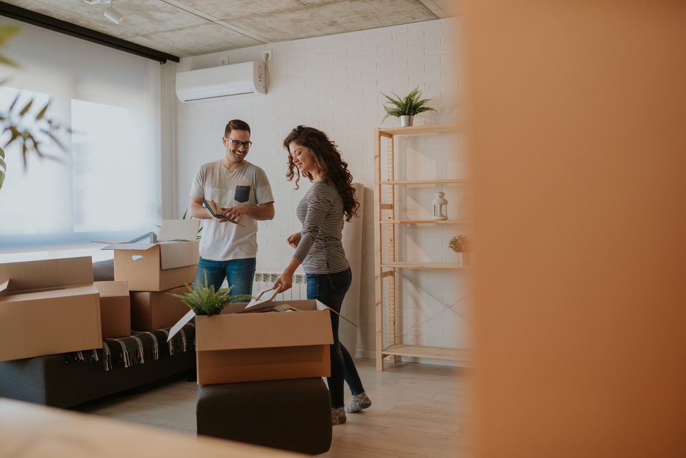 Photo of good looking young couple having fun while unpacking boxes in new rental home on moving day. Young couple is moving in to their new rental home and transferred their rental insurance.