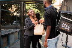 Office food delivery service courier giving customer order package. Man holding restaurant takeaway meal, happy cheerful company employee taking lunch paper bag, car insurance for delivery drivers.