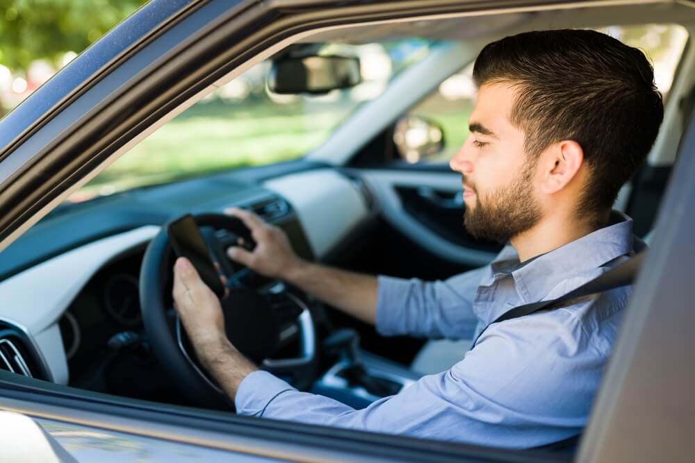 Rideshare gig worker checks his app to see if he has a ride to pick up, rideshare and delivery car insurance.