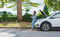 Woman using mobile phone calling for roadside assistance after a car breakdown on street. Concept of vehicle engine problem or accident and emergency help from professional mechanic and cheap roadside assistance.