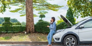 Woman using mobile phone calling for roadside assistance after a car breakdown on street. Concept of vehicle engine problem or accident and emergency help from professional mechanic and cheap roadside assistance.