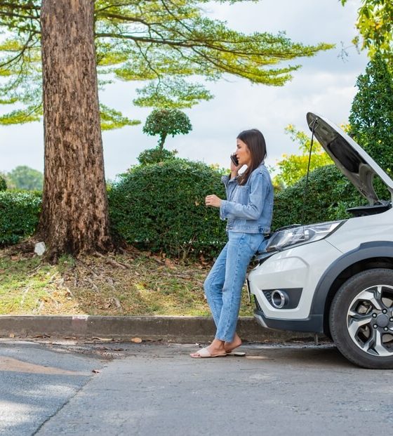 Woman using mobile phone calling for roadside assistance after a car breakdown on street. Concept of vehicle engine problem or accident and emergency help from professional mechanic and cheap roadside assistance.