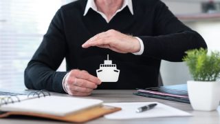 Insurer protecting a paper boat with his hand, concept of boat insurance.