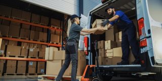 Outside of logistics distributions warehouse: diverse team of workers use hand truck loading delivery van with cardboard boxes, online orders, e-commerce purchases. Concept of when commercial auto insurance is right for you.
