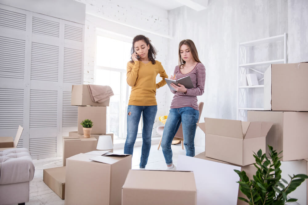 Young roommates unpacking their belongings in their new apartment, checking an inventory list for their cheap renters insurance.