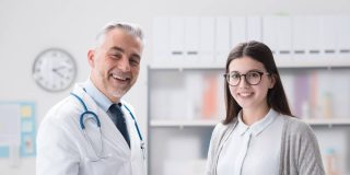 Man doctor smiling next to his female patient holding documents of her policy after learning how to successfully apply to the Covered California open enrollment process.