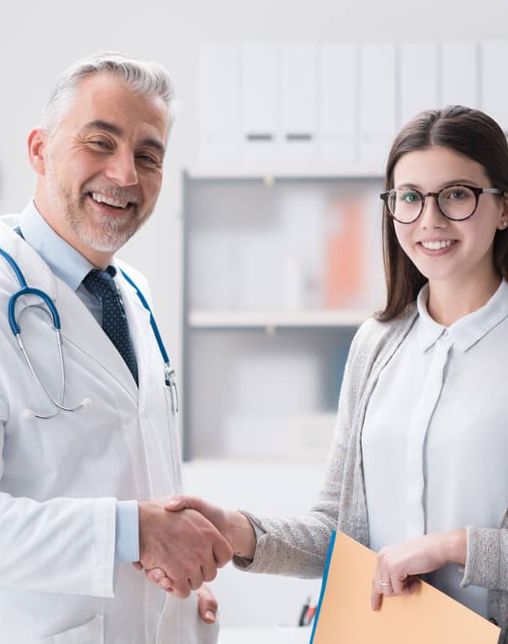 Man doctor smiling next to his female patient holding documents of her policy after learning how to successfully apply to the Covered California open enrollment process.