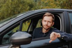 An unhappy driver gives a thumbs down in their car, reflecting common auto insurance mistakes.