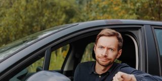 An unhappy driver gives a thumbs down in their car, reflecting common auto insurance mistakes.