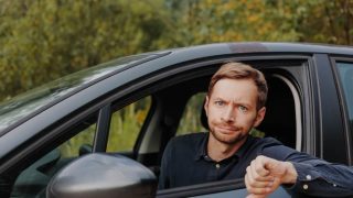 An unhappy driver gives a thumbs down in their car, reflecting common auto insurance mistakes.