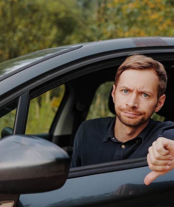 An unhappy driver gives a thumbs down in their car, reflecting common auto insurance mistakes.