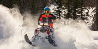 Young man driving a snowmobile in motion on a beautiful winter day, highlighting snowmobile insurance.