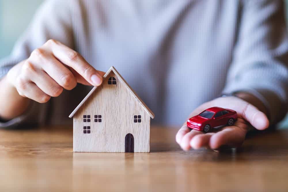 Woman holding small house and car models to illustrate the benefits of bundling auto and homeowners insurance